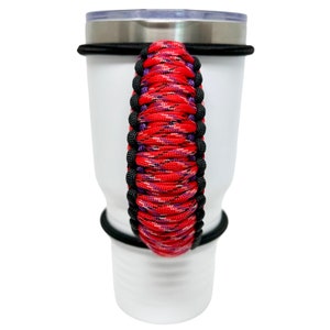 May include: A white tumbler with a red, black, and purple paracord handle. The handle is wrapped around the tumbler and secured with black bands.