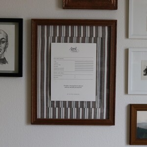 Pu&ograve; includere: Una collezione di opere d'arte incorniciate su un muro bianco. L'arte comprende un ritratto a matita, un documento con testo e schizzi di paesaggi e figure. Le cornici sono di varie dimensioni e colori, tra cui nero e marrone.