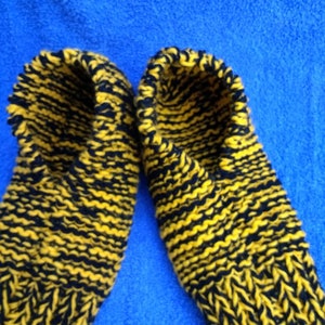 May include: A pair of knitted slippers in black and yellow. The slippers are made with a thick yarn and have a simple design.