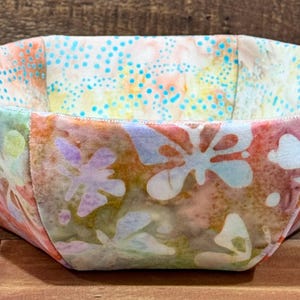 May include: A fabric bowl with a colorful floral pattern in shades of pink, blue, green, and yellow. The bowl is made of fabric and has a unique octagonal shape.