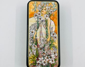May include: A rectangular wooden box with a black border and a colorful image of a woman standing in a field of white flowers. The woman is wearing a white dress and has long blonde hair. The flowers are painted in shades of pink, yellow, and green.
