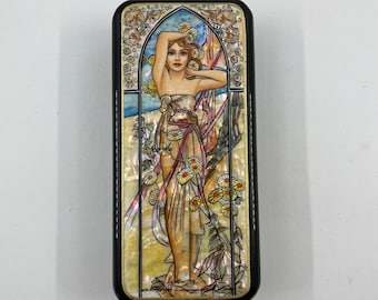 May include: Rectangular black box with a decorative Art Nouveau design. The design features a woman with long hair, adorned with flowers, standing in front of a window. The artwork has a mother-of-pearl effect with yellow, white, and blue accents.