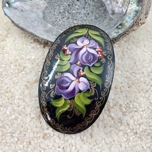 May include: An oval-shaped wooden trinket box with a black background and a hand-painted design of purple flowers with green leaves and gold accents.