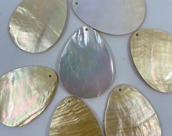 May include: A collection of seven teardrop-shaped mother-of-pearl pendants, each featuring a small drilled hole at the top. The pieces display iridescent, pearlescent surfaces with varying shades of cream, white, and soft golden yellow tones.