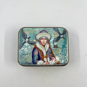 May include: A hand-painted wooden box with a winter scene featuring a woman in a white fur-trimmed hat and coat, holding a red bird. Two magpies fly above her in a snowy forest. The box is signed "Снегурочка" and "Зографыня".