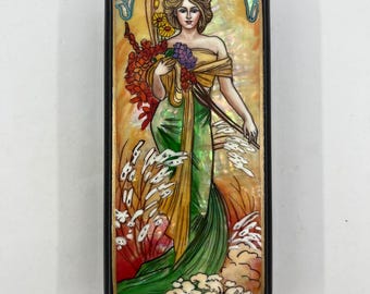 May include: Rectangular decorative box with a black frame. The box features an Art Nouveau style illustration of a woman in a flowing green and yellow dress, holding flowers. The background is a mix of orange, yellow, and white, with the artist's signature at the bottom.