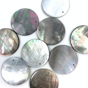 Può includere: Una collezione di nove ciondoli circolari in madreperla, ognuno caratterizzato da un riflesso iridescente unico con varie tonalità di grigio, bianco e rosa. Ogni disco piatto e rotondo presenta un piccolo foro vicino al bordo per l'aggancio.