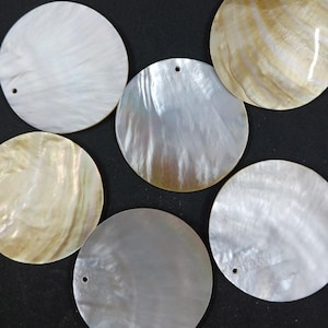 May include: A collection of six iridescent, round mother-of-pearl shell pendants. Each pendant has a small hole for stringing and displays a range of colors, including white, cream, and silver, with natural patterns.