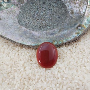 May include: A smooth, oval-shaped, red carnelian gemstone pendant with a hole drilled through the top for stringing.