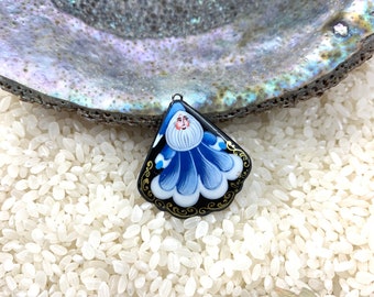 May include: A hand-painted pendant featuring a stylized figure with a white beard and blue robes. The pendant has a black border with gold accents and a small metal loop at the top. The background is white rice.