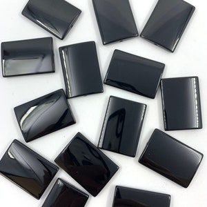 May include: A group of 12 black rectangular shaped beads. The beads are smooth and glossy.