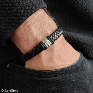 May include: A black leather bracelet with a silver cross accent. The bracelet is braided and has a magnetic clasp.