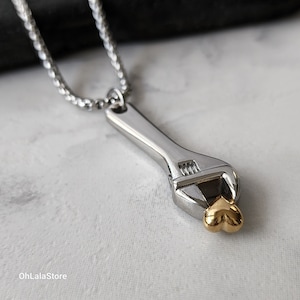 May include: A silver adjustable wrench necklace with a gold heart charm. The wrench is a popular symbol of love and support for those who work with their hands.