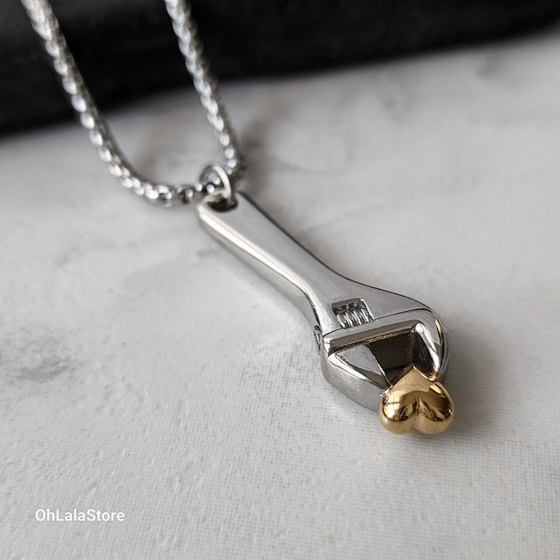 May include: A silver adjustable wrench necklace with a gold heart charm. The wrench is a popular symbol of love and support for those who work with their hands.
