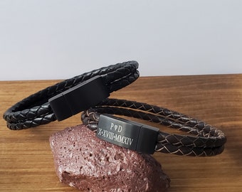 May include: Two black leather bracelets with a black metal clasp. The bracelet on the bottom has the inscription "P&D X-XVIII-MMXIV".