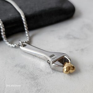 May include: A silver necklace with a wrench pendant. The wrench has a gold heart at the end.