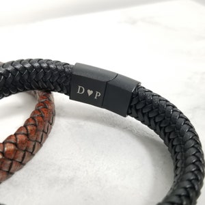 Pu&ograve; includere: Braccialetto in pelle nera con design intrecciato e chiusura in metallo nero. La chiusura &egrave; incisa con le iniziali "D&hearts;P".
