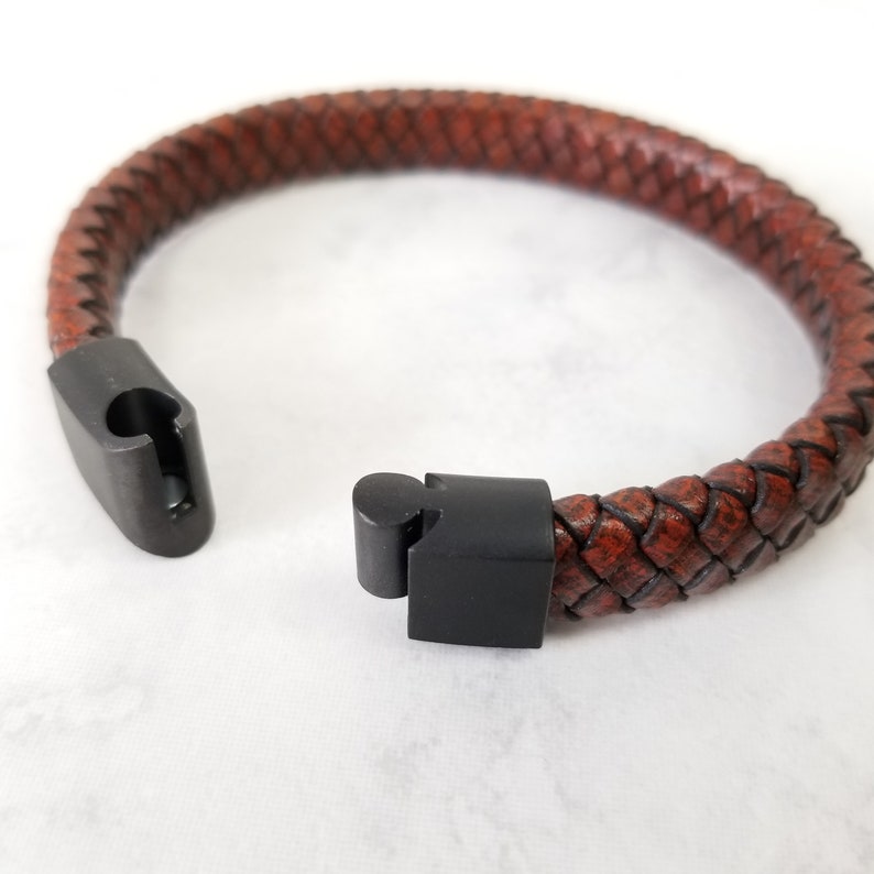 Pu&ograve; includere: Un braccialetto in pelle marrone con una chiusura in metallo nero. Il braccialetto &egrave; intrecciato e ha un design semplice.