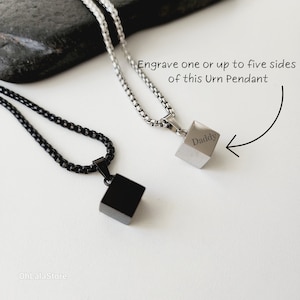 May include: Two silver necklaces with cube-shaped pendants. The pendant on the right has the word "Daddy" engraved on it. The text "Engrave one or up to five sides of this Urn Pendant" is written above the pendant.