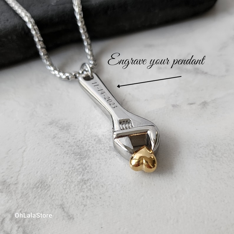 May include: Silver adjustable wrench pendant necklace with a gold heart at the end. The pendant is engraved with the date "11-14-2023".