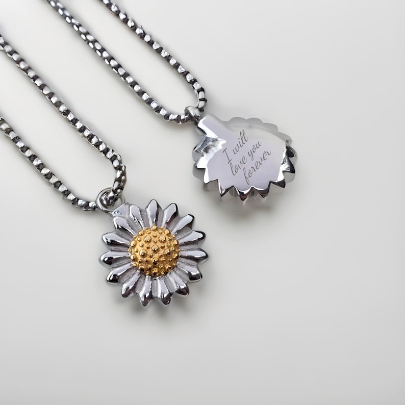 K&ouml;nnte beinhalten: Zwei silberne Halsketten mit Sonnenblumenanh&auml;ngern. Ein Anh&auml;nger hat eine goldene Mitte und der andere hat die Worte "Ich werde dich f&uuml;r immer lieben" auf der R&uuml;ckseite graviert.