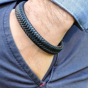 Pu&ograve; includere: Un braccialetto in pelle intrecciata nero indossato al polso.