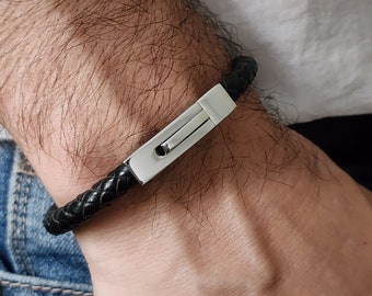 May include: Black braided leather bracelet with a silver-tone clasp. The bracelet is shown on a wrist, showcasing the texture of the leather and the sleek design of the clasp. A stylish accessory.