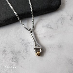 May include: A silver necklace with a silver wrench pendant holding a gold heart charm.