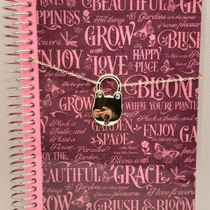 May include: A pink and purple spiral bound journal with a gold lock and chain. The cover features a floral pattern with butterflies and the words "Enjoy the little things", "Beautiful", "Grow with Love", "My Happy Place", "Bloom", "Garden", "Spade", "Bloom with Grace", "Blush & Bloom", and "Grow".