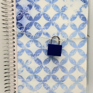 May include: A white spiral bound journal with a blue and white watercolor pattern. The journal is closed and secured with a silver chain and a blue padlock.