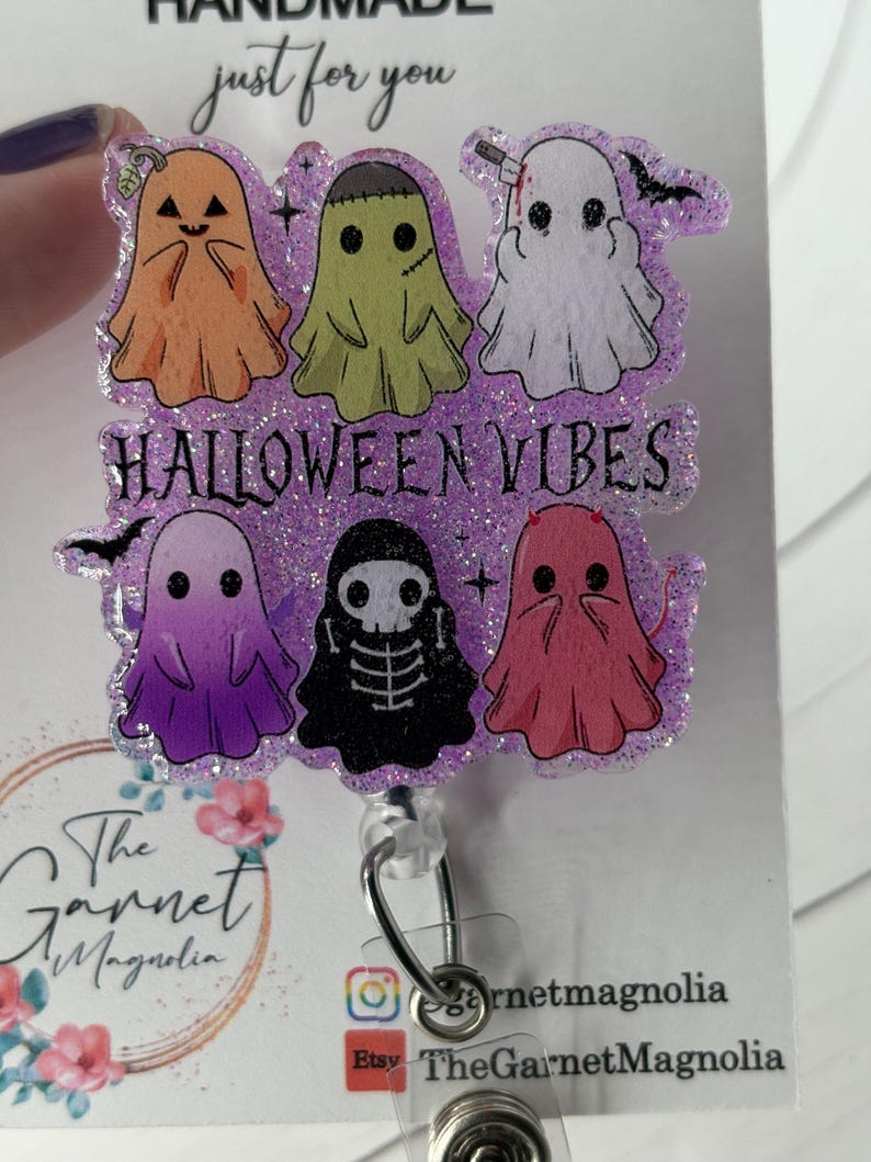 May include: A Halloween-themed badge reel featuring six cartoon ghosts in various colors, including orange, green, white, purple, black, and pink. The phrase "HALLOWEEN VIBES" is displayed across the center. The badge reel has a glittery purple border.