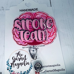 May include: Pink glitter brain-shaped badge holder with the text "Stroke Team" in black lettering. The badge holder is attached to a clear plastic badge reel with a silver clip. The badge holder is handmade and has a small floral design on the back.