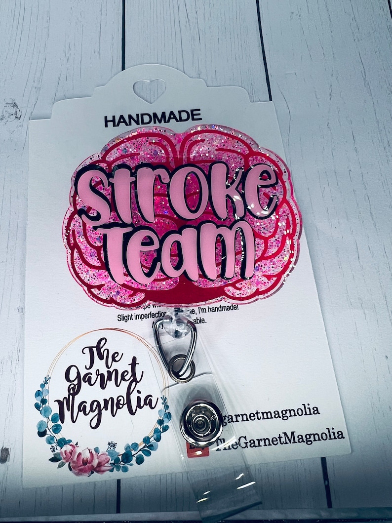 May include: Pink glitter brain-shaped badge holder with the text "Stroke Team" in black lettering. The badge holder is attached to a clear plastic badge reel with a silver clip. The badge holder is handmade and has a small floral design on the back.