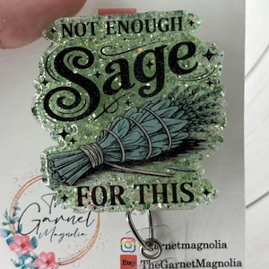 May include: A glittery badge reel with the words "NOT ENOUGH Sage FOR THIS" in black script. The badge features a bundle of sage in blue-green, with a silver reel clip and a floral logo.
