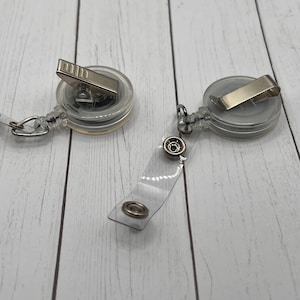 May include: Two clear retractable badge holders with silver clips and a clear strap with silver rings.