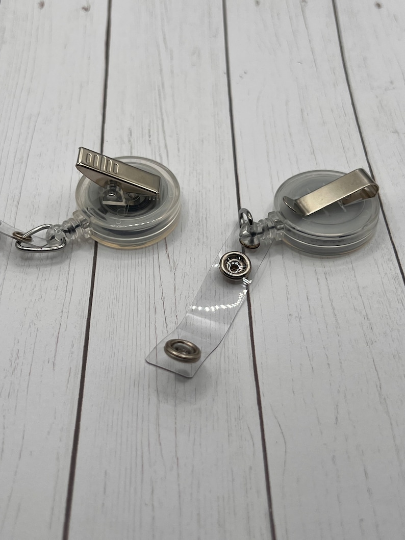 May include: Two clear retractable badge holders with silver clips and a clear strap with silver rings.
