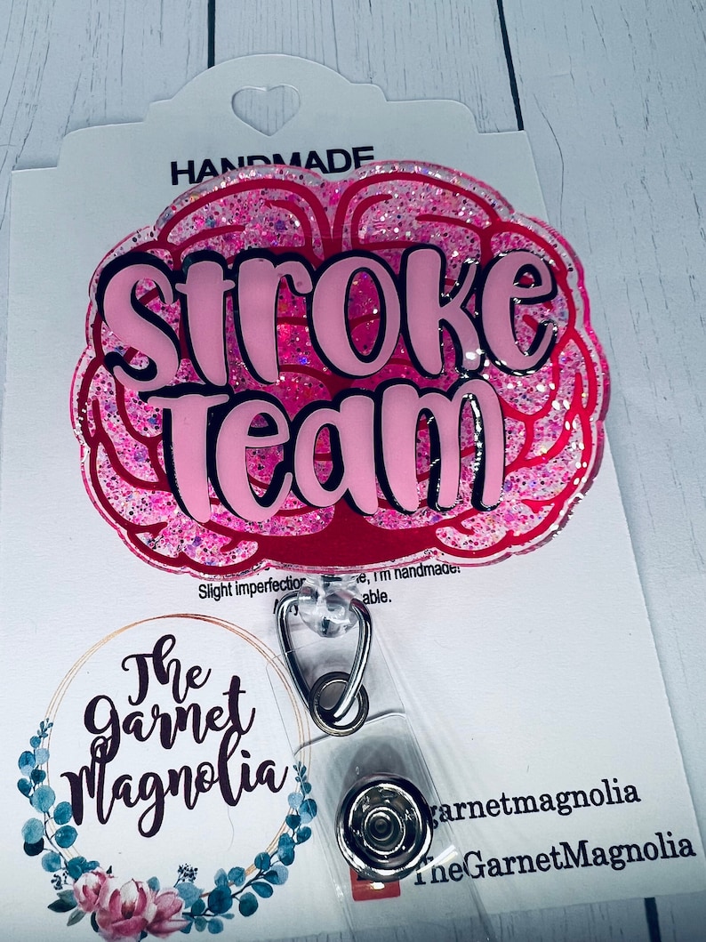 May include: Pink glitter brain-shaped badge holder with the text "Stroke Team" in black and pink lettering. The badge holder is attached to a clear plastic retractable badge reel with a silver clip.