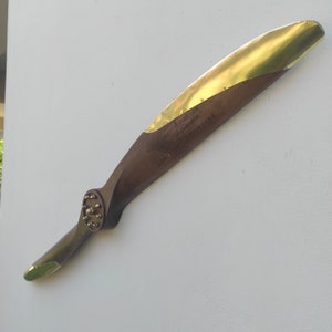 Könnte beinhalten: Ein hölzerner Flugzeugpropeller im Vintage-Stil mit Messingakzenten. Der Propeller hat eine dunkelbraune Oberfläche mit Messingkanten an den Spitzen und der Vorderkante. Text ist sichtbar, darunter "Aviation of London" und "1934".