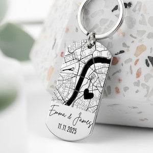 Könnte beinhalten: Ein silberfarbener Schlüsselanhänger mit einem schwarz-weißen Kartendesign. Die Karte zeigt einen Fluss und ein Herzsymbol. Die Namen "Emma & James" und das Datum "11.11.2025" sind auf dem Schlüsselanhänger eingraviert.