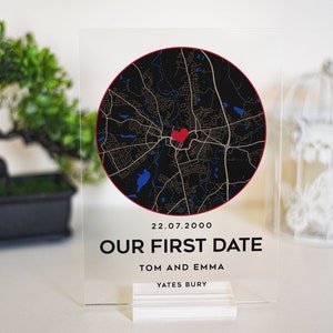 May include: A clear acrylic sign with a black and white map of a city with a red heart in the center. The text on the sign reads "22.07.2000 Our First Date Tom and Emma Yates Bury".