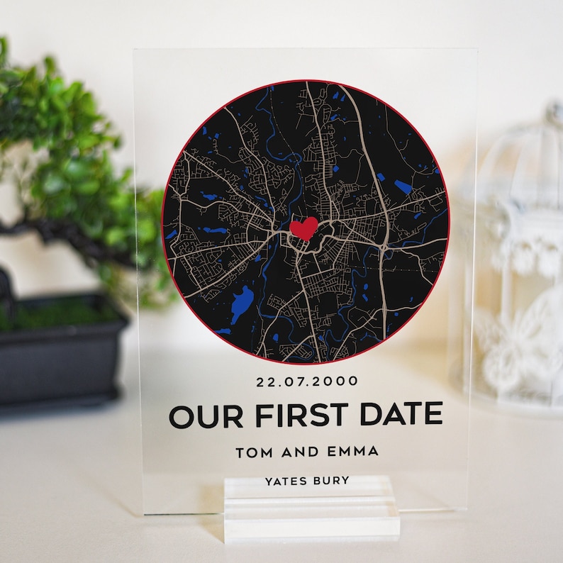 May include: A clear acrylic sign with a black and white map of a city with a red heart in the center. The text on the sign reads "22.07.2000 Our First Date Tom and Emma Yates Bury".