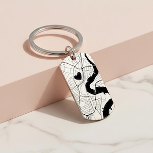 May include: A rectangular keyring featuring a black and white map design. The keyring has a silver ring and a heart symbol on the map. The map depicts streets and a river.