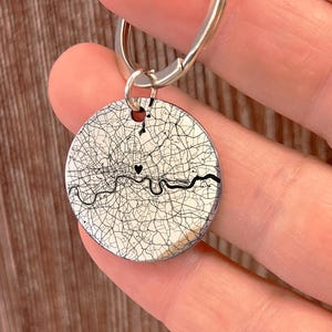 May include: A silver keyring with a circular pendant showing a detailed map of London. The map is in black and white, with a heart symbol marking a location. The River Thames is visible. A silver key ring is attached.