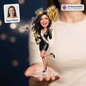 Peut inclure: Figurine de dessin animé personnalisée d'une femme célébrant son 40e anniversaire. Elle porte une robe noire à paillettes, une écharpe avec l'inscription "40 & Fabulous" et tient une bouteille de champagne et des ballons dorés. Une photo de femme est à gauche.