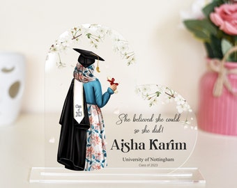 May include: A clear acrylic graduation keepsake featuring a graduate in a hijab, cap, and gown, holding a diploma. The design includes floral accents and the text "She believed she could so she did!" with a name and university details.