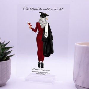 May include: A graduation acrylic plaque with a red and black illustration of a woman wearing a graduation cap and gown. The text "She believed she could, so she did" is at the top of the plaque. The text "Zarah Hussain, University of Nottingham, Class of 2022" is at the bottom of the plaque.