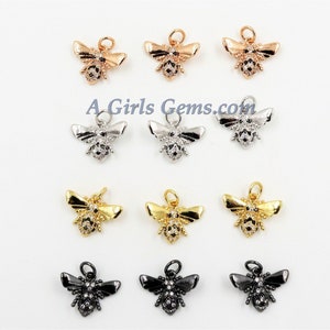 May include: Twelve bee charms in various finishes, including gold, silver, rose gold, and black. The charms are all the same design, with a detailed bee shape and a loop for attaching to jewelry.