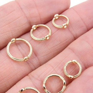 May include: Six gold-toned hoop earrings with small clear stones on each side. The hoops are of varying sizes.