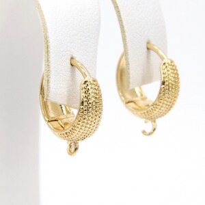 May include: A pair of gold hoop earrings with a textured surface. The earrings have a small loop at the bottom.