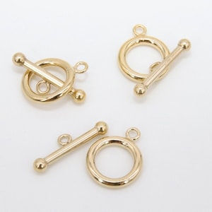May include: Three gold-toned metal toggle clasps for jewelry making. Each clasp features a round ring and a straight bar.